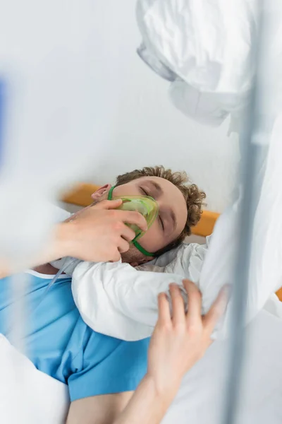 Врач в защитном костюме осматривает пациента в кислородной маске в больнице — стоковое фото