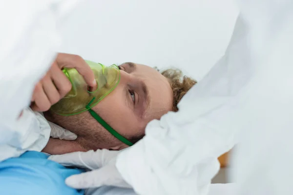 Doctor in hazmat suit and latex gloves examining patient in oxygen mask in hospital — Stock Photo