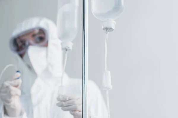 Doctor in personal protective equipment and goggles holding catheter on drop counter — Stock Photo