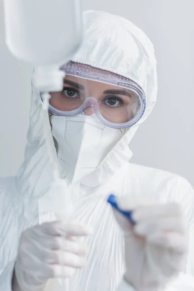 Médico en traje de materiales peligrosos y gafas que sostienen el catéter en el mostrador de gotas — Stock Photo