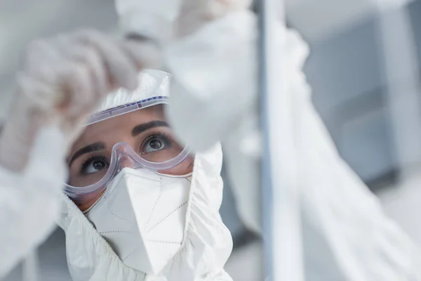 Médico en traje de materiales peligrosos, máscara médica y gafas que sostienen el catéter en el mostrador de gotas - foto de stock