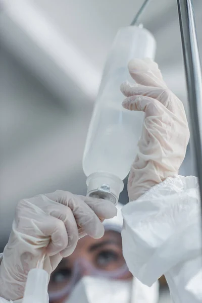 Vista recortada del médico en guantes de látex que sostienen el catéter en el contador de gotas - foto de stock