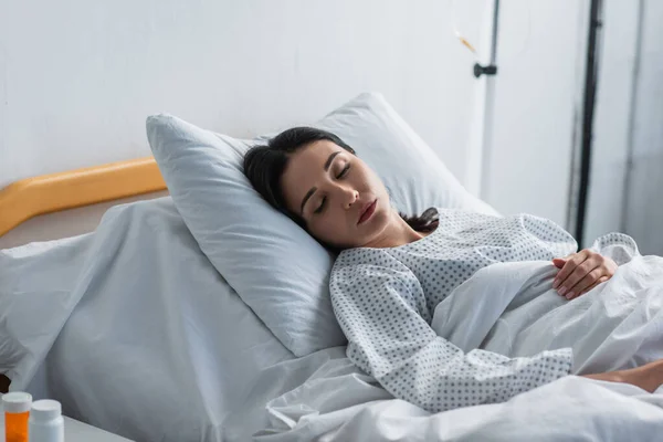 Morena mujer en vestido de paciente acostado en la cama del hospital - foto de stock