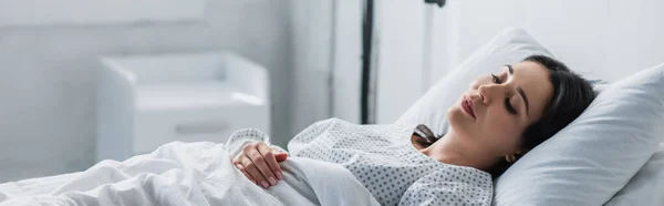 Morena mujer en vestido de paciente acostado en la cama del hospital, pancarta - foto de stock