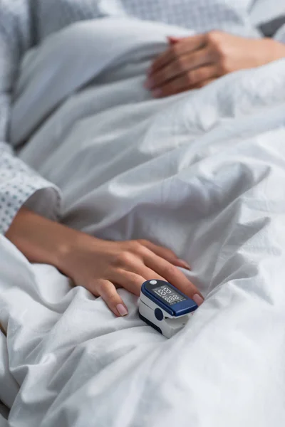 Vista ritagliata della donna con ossimetro sul dito sdraiato sul letto di ospedale — Foto stock