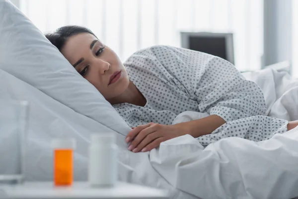 Mujer enferma mirando botellas borrosas con medicamentos - foto de stock