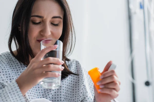 Woman holding bottle with medication while taking pill in hospital — Stock Photo