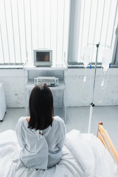 Back view of woman in patient gown sitting on hospital bed — Stock Photo