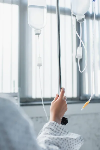 Vista recortada de la mujer enferma cogida de la mano en el mostrador de gota con frascos de terapia intravenosa - foto de stock