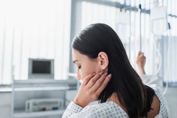 Mujer enferma ajustando el cabello mientras toma de la mano en el mostrador de gota con botellas de terapia intravenosa - foto de stock