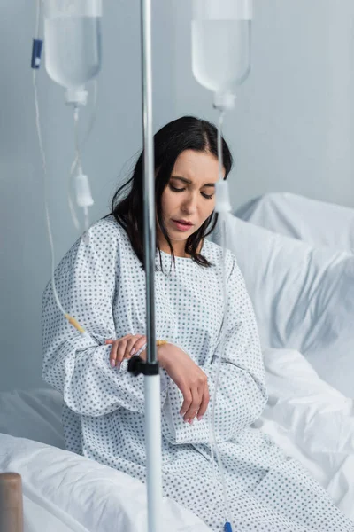 Mujer enferma que mira el catéter durante la terapia en el hospital - foto de stock