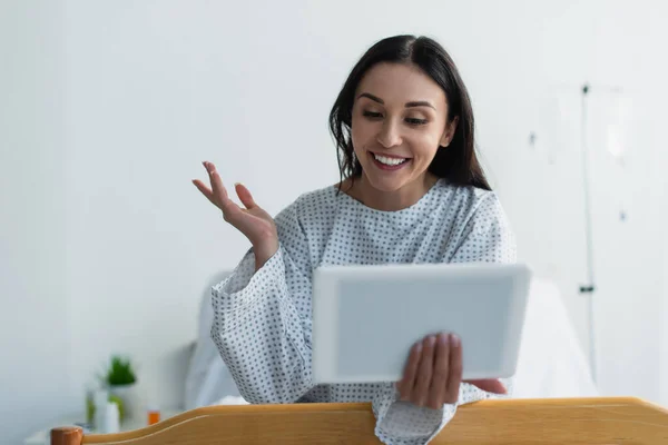 Lächelnde Frau im Patientenkleid gestikuliert bei Videoanruf im Krankenhaus — Stockfoto