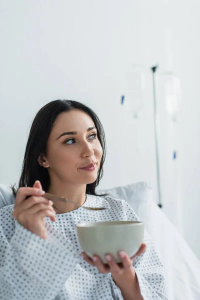 Paciente pensativo sosteniendo cuchara y tazón con desayuno en el hospital - foto de stock