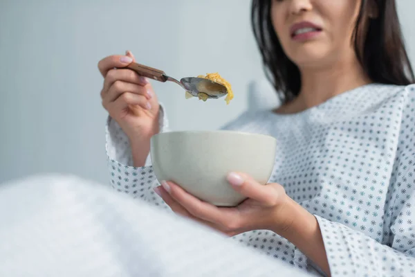 Vue recadrée du patient dégoûté tenant une cuillère avec des flocons de maïs et un bol à l'hôpital — Photo de stock