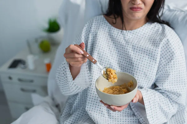 Partial view of disgusted woman holding spoon with corn flakes and bowl in hospital — Stock Photo