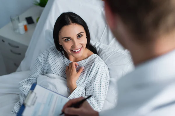 Visão de alto ângulo de mulher sorridente olhando para médico desfocado prescrição de escrita — Stock Photo