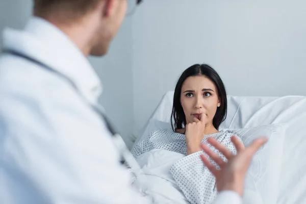 Femme brune en robe de patient regardant le médecin flou à l'hôpital — Photo de stock