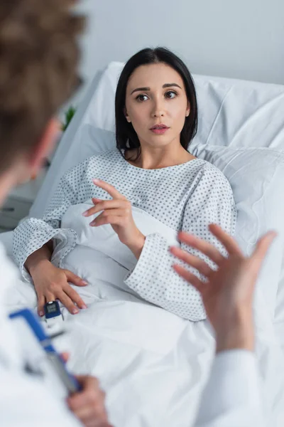 Brunette woman in patient gown looking at blurred doctor in clinic — Stock Photo