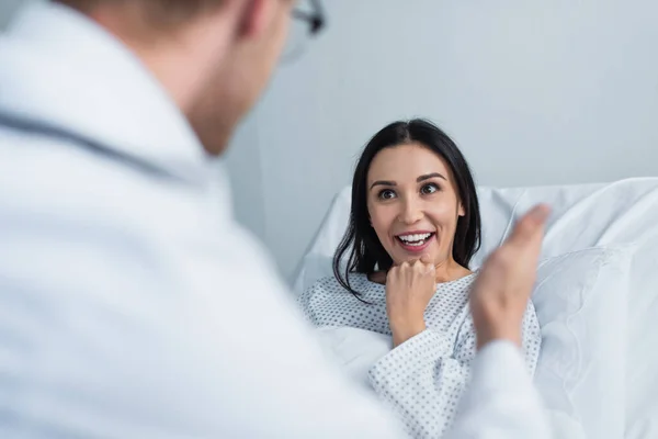 Brunette patient smiling while looking at blurred doctor in clinic — Stock Photo