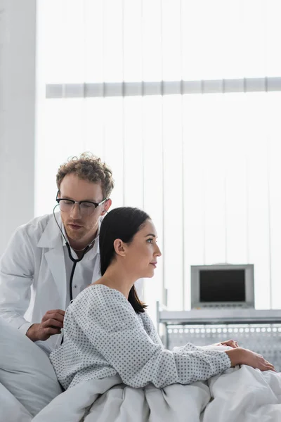 Кудрявый доктор в очках, осматривает брюнетку в больнице — стоковое фото