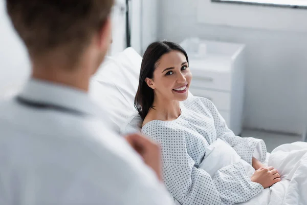 Mulher positiva em vestido paciente olhando para médico desfocado em casaco branco — Fotografia de Stock