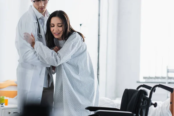 Doctor in glasses helping woman near wheelchair — Stock Photo