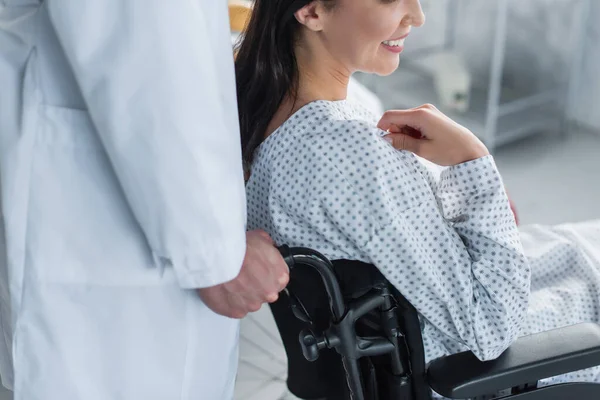 Cropped view of doctor in white coat standing behind smiling disabled woman in wheelchair — Stock Photo