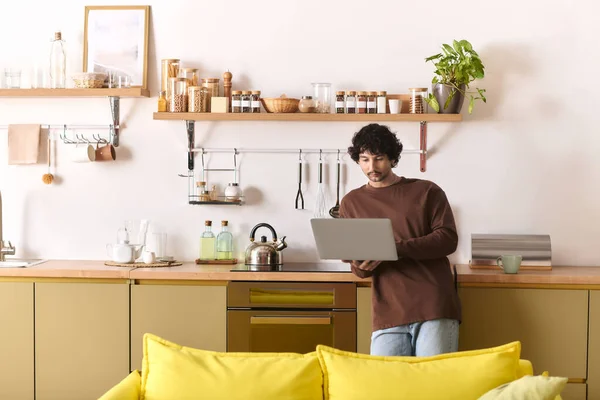 A young man engages with his laptop while standing in a modern kitchen filled with natural light. — Stock Photo