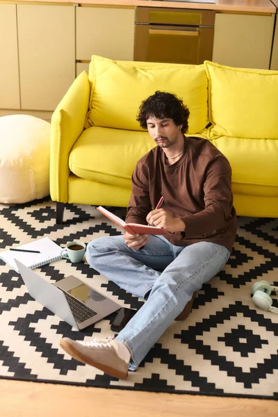 A young man sits on the floor, surrounded by a vibrant yellow couch and warm decor, sketching ideas. — Stock Photo