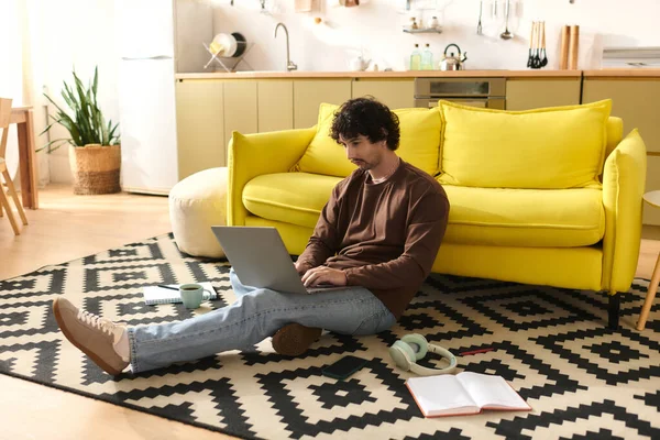 Handsome man sits on the floor, focused on laptop in a warm home setting with lively decor. - foto de stock