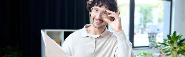 Handsome young man with curly hair and glasses enjoys a moment of joy in his workspace. — Stockfoto