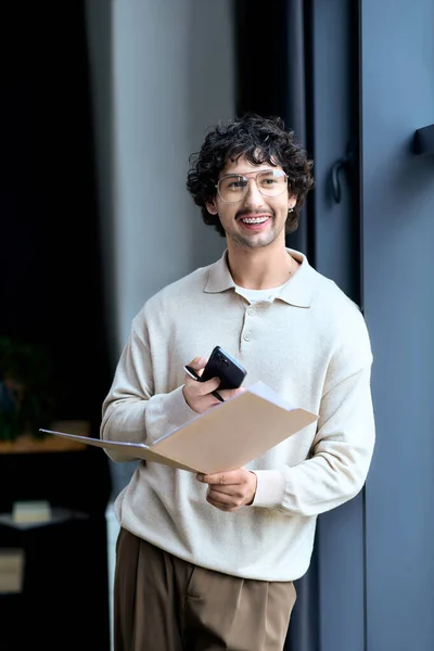 Young man enjoys a moment in a stylish space, holding a folder and smiling at his phone. — стокове фото
