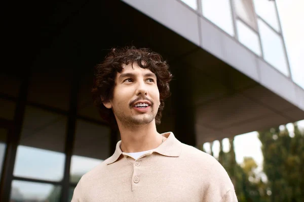 Young man stands outdoors, smiling brightly in front of a contemporary structure on a sunny day. — стоковое фото