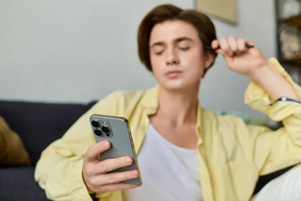 El hombre de moda se sienta cómodamente en un sofá revisando su teléfono inteligente en una sala de estar moderna. - foto de stock