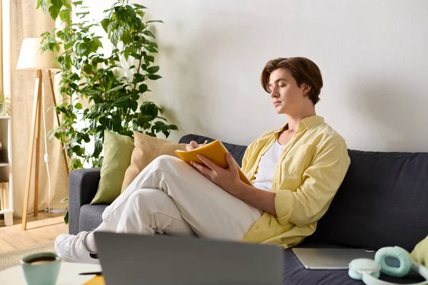 Un jeune homme élégant s'assoit confortablement sur un canapé, écrivant des notes dans une pièce lumineuse et accueillante. — Photo de stock