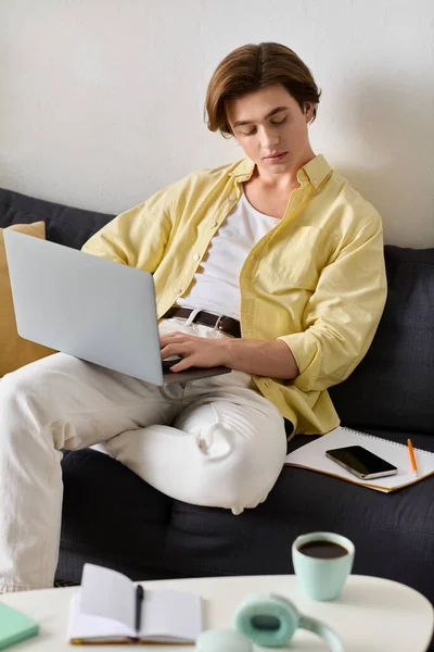 Jovem elegante relaxa em um sofá, focado em seu laptop com café e notas nas proximidades. — Fotografia de Stock