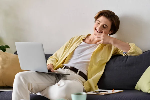 Fashionable young man smiles while using his laptop, surrounded by a warm and inviting space. — Stock Photo