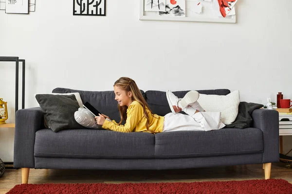 Девушка отдыхает на уютном диване дома, занимаясь планшетом в свободное время. — стоковое фото