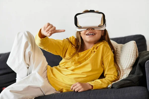 Une fille alpha de génération se détend sur le canapé à la maison, portant un casque VR et souriant joyeusement. — Photo de stock