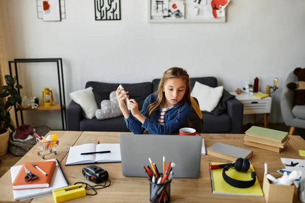 Ein junges Mädchen sitzt an einem Tisch, umgeben von Büchern und Vorräten, konzentriert auf ihren Laptop.. — Stockfoto