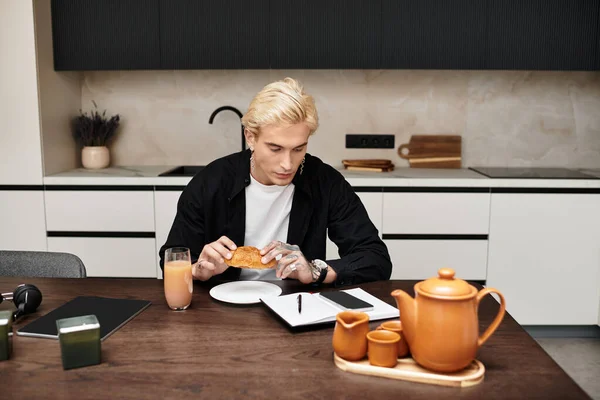 На стильной кухне молодой человек пьет сок и пишет заметки, находя вдохновение в своей закуске.. — стоковое фото