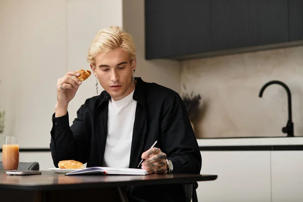 Giovane bell'uomo prende un momento per godersi un croissant e note in un appartamento luminoso. — Foto stock