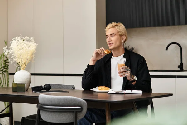 Красивый молодой человек сидит за современным столом, наслаждаясь закусками и напитками на завтрак. — стоковое фото