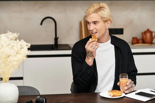 Красивый молодой человек расслабляется на стильной кухне, наслаждаясь выпечкой и соком во время утреннего блаженства. — стоковое фото