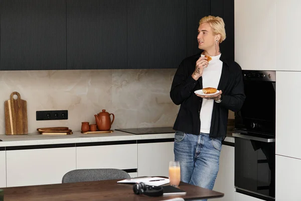 Um homem jovem e atraente está em sua cozinha moderna saboreando uma deliciosa massa com suco de laranja. — Fotografia de Stock