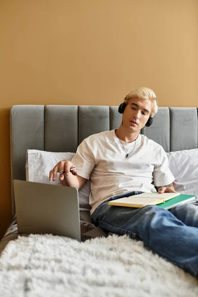 A young man relaxes on his bed, focusing on a laptop while surrounded by study materials. — Stock Photo
