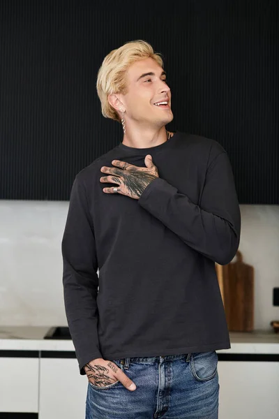 Un jeune homme aux cheveux blonds et tatoués exprime son bonheur dans un cadre élégant et moderne de cuisine. — Photo de stock