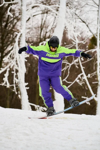 Un uomo barbuto compie un trucco elegante mentre fa snowboard su un pendio fresco e innevato. — Foto stock