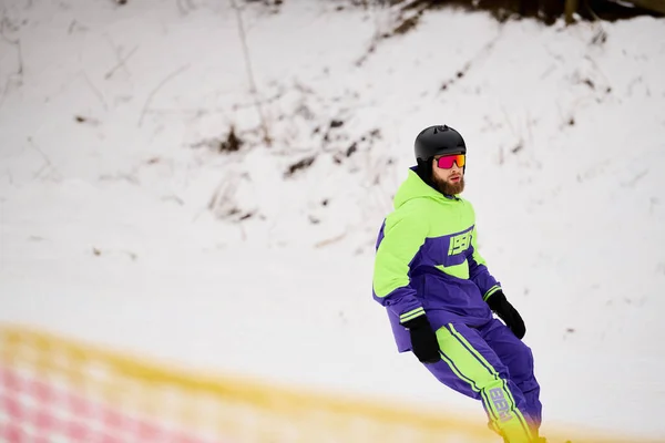 Ein bärtiger Mann genießt an einem Wintertag das Snowboarden auf einem schneebedeckten Hang, trägt helle Kleidung. — Stockfoto