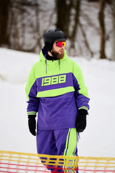 Ein bärtiger Mann fährt einen schneebedeckten Hang hinunter und zeigt seine Snowboard-Fähigkeiten in heller Kleidung. — Stockfoto